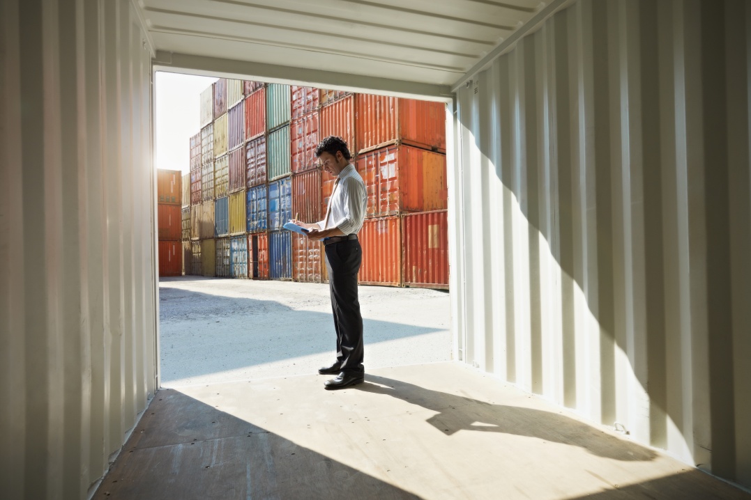 portrait of mid adult businessman standing near cargo container and writing on clipboard. Horizontal shape, side view, copy space