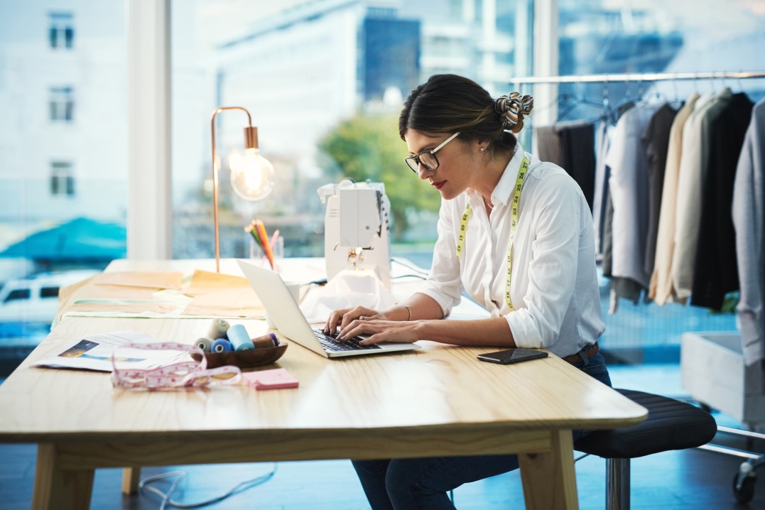 Diseñadora de moda, mujer y tecleando en portátil en tienda para email, proyecto o pedido online de tela en startup creativa. Sastre serio, ordenador y pequeño negocio de ropa o .textil en boutique